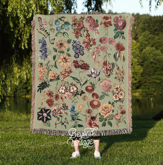 a woman standing in the grass holding a blanket with flowers on it