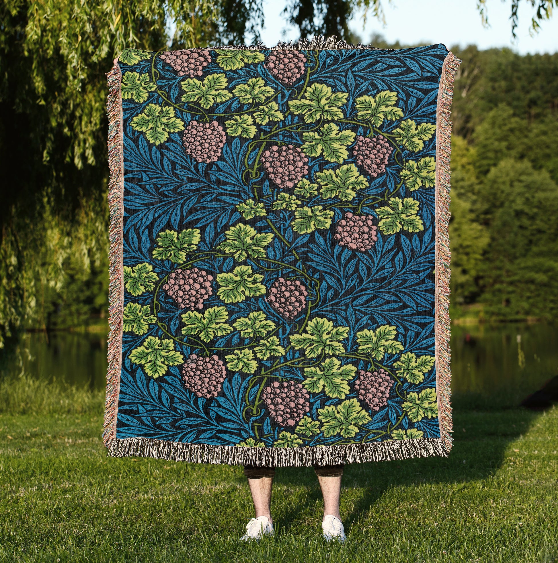 a woman standing in the grass holding a blue and green quilt