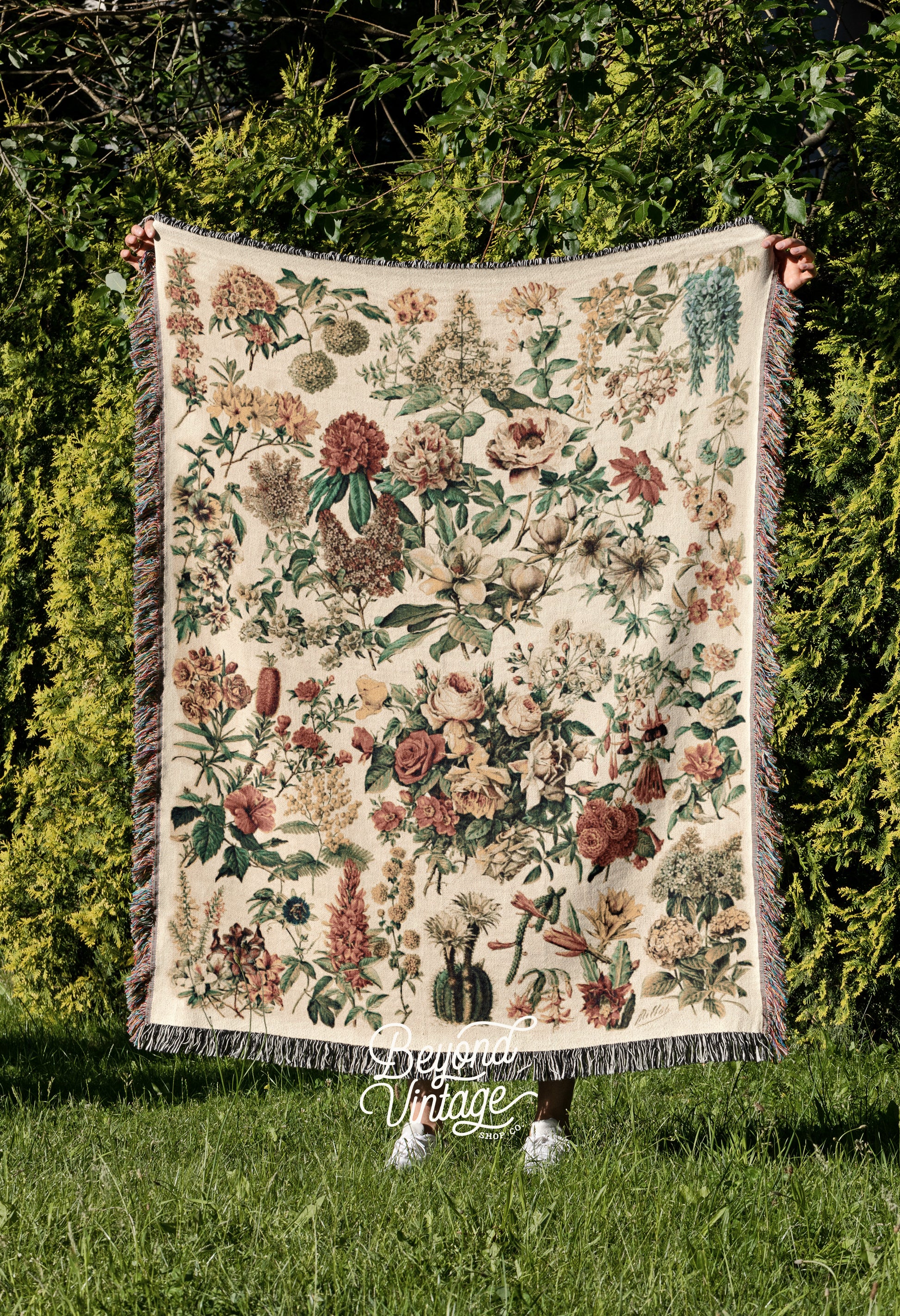 a woman holding up a tapestry in front of a hedge