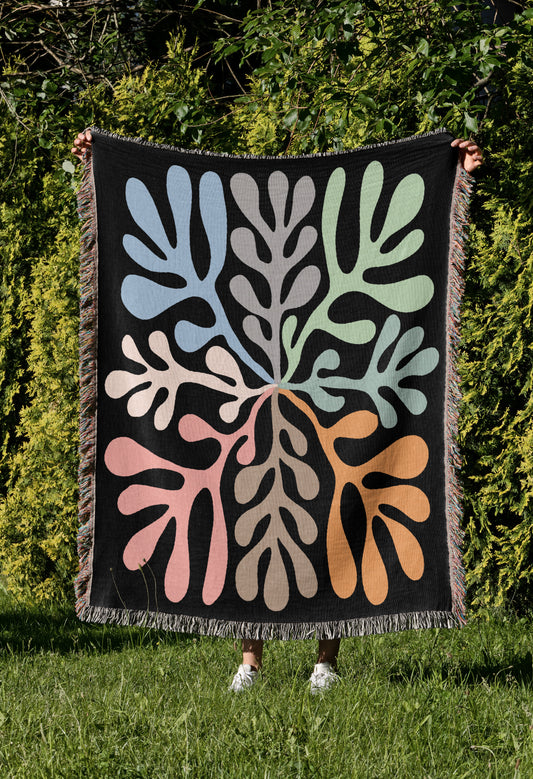 a woman holding up a black quilt with colorful leaves on it