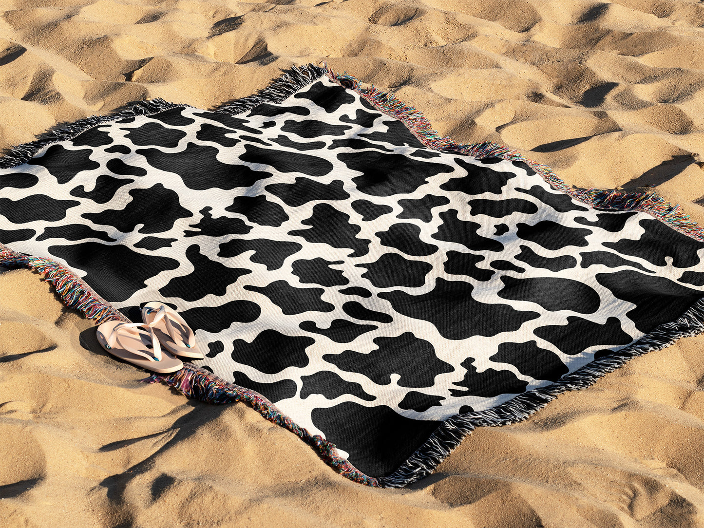 a black and white cow print blanket laying in the sand