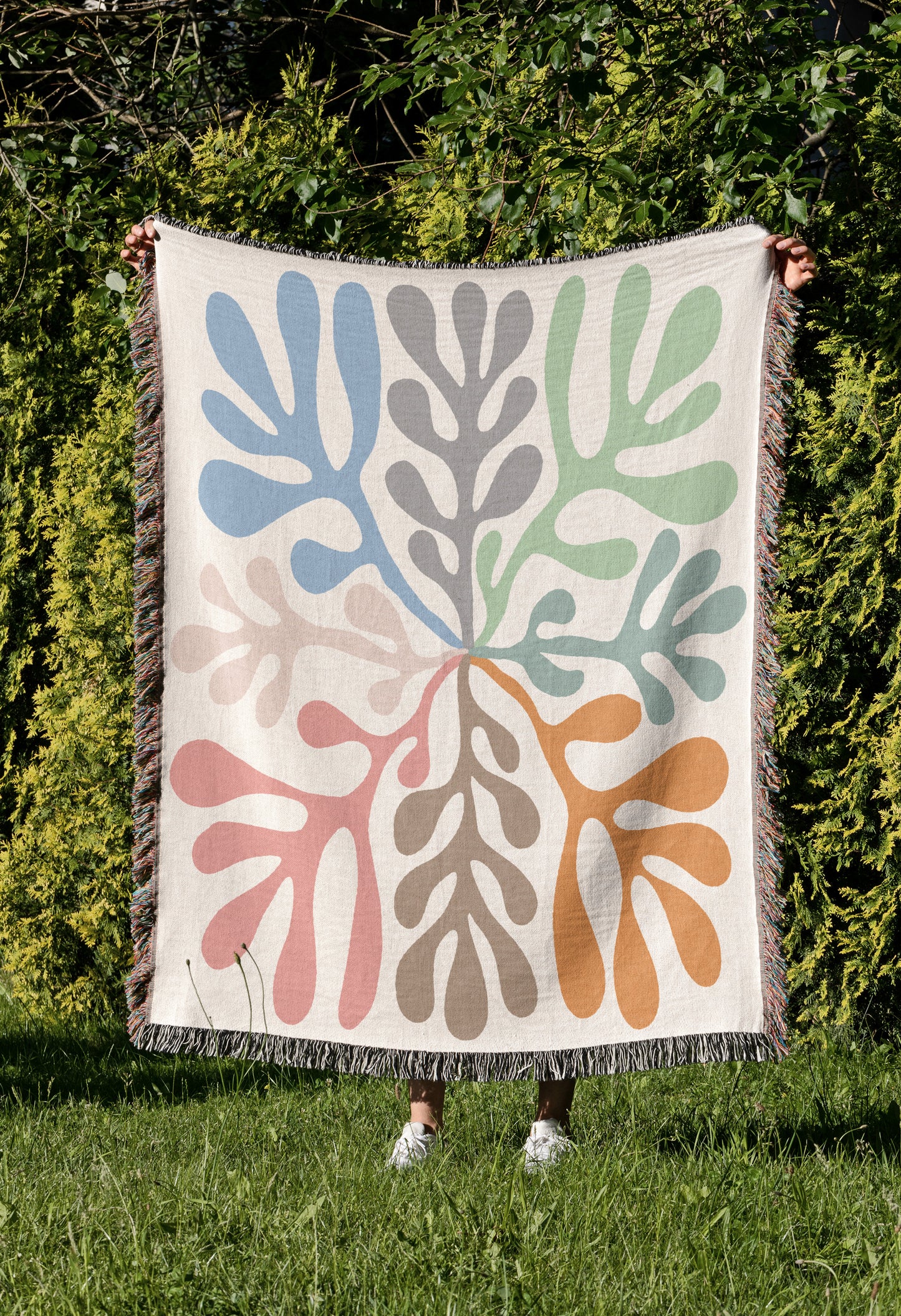 a woman holding up a colorful tapestry in front of a bush