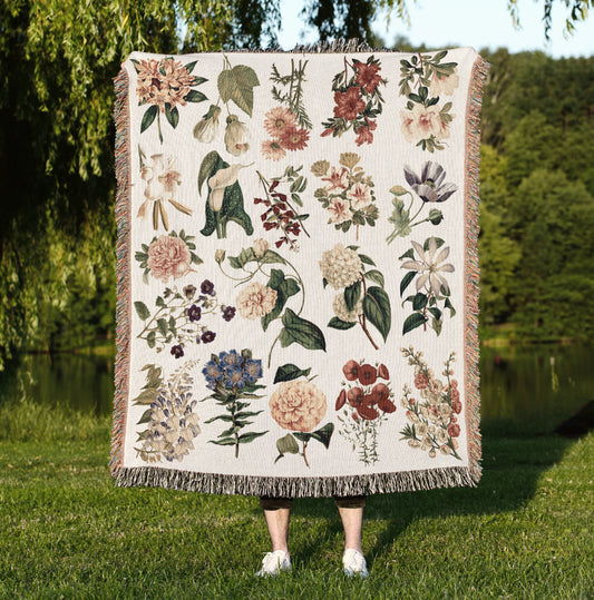 a woman standing in the grass holding a blanket with flowers on it