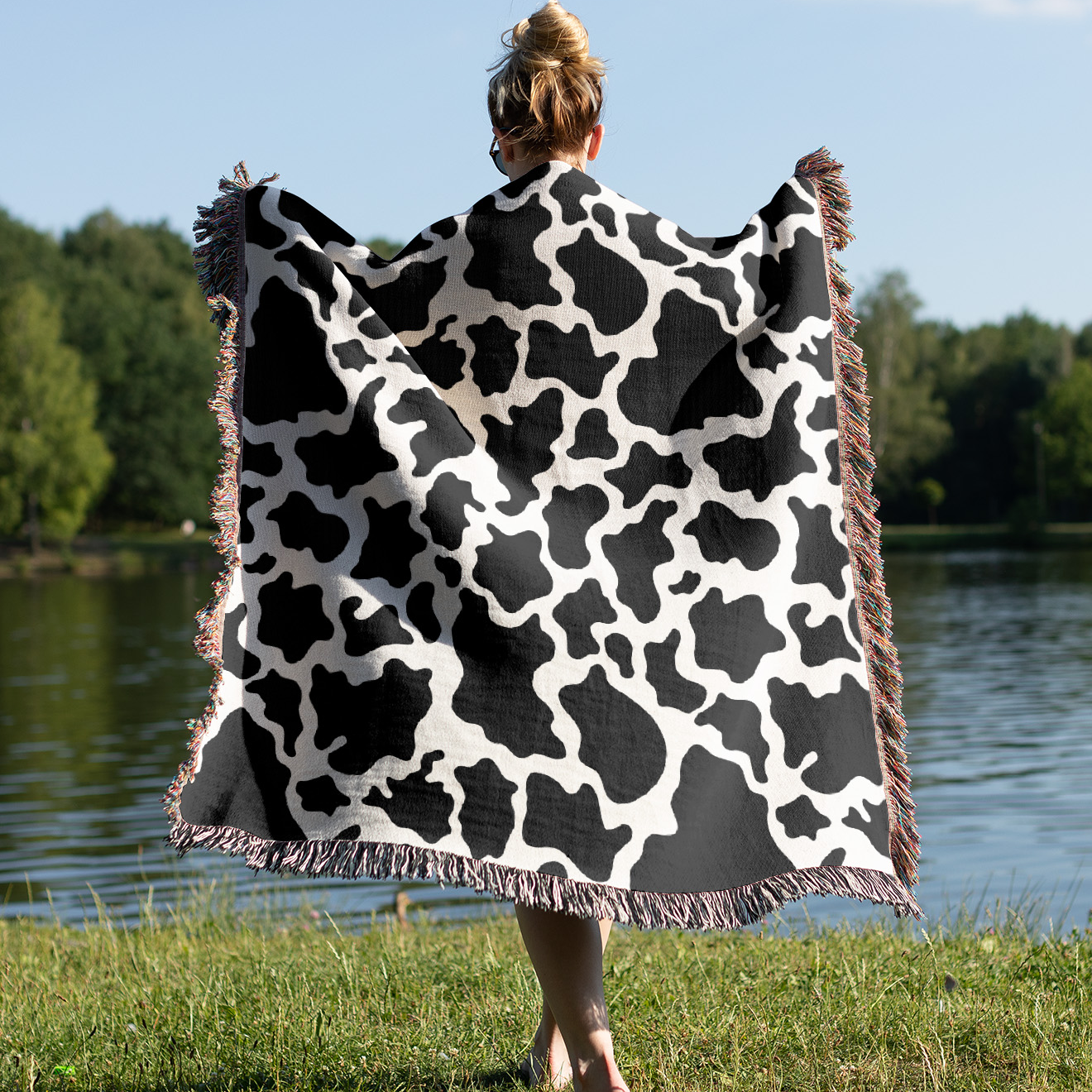 a woman holding a cow print blanket in front of a lake